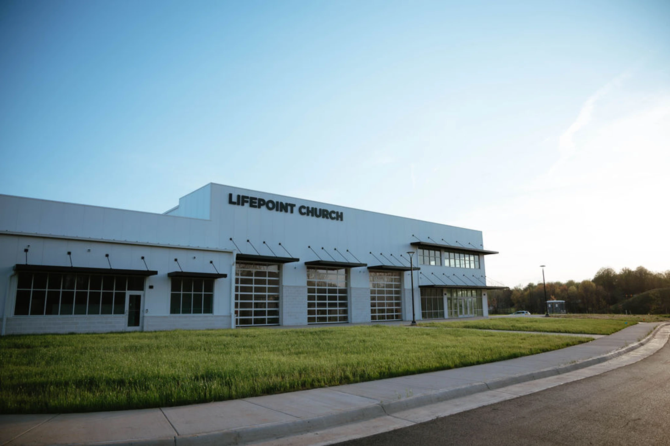 A wide shot of the modern, white Lifepoint Church building with large windows and glass garage doors, set against a clear blue sky on a sunny day.
