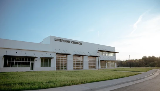 The modern, white exterior of LifePoint Church, featuring large windows and glass garage doors, set against a clear sky during sunrise or sunset.