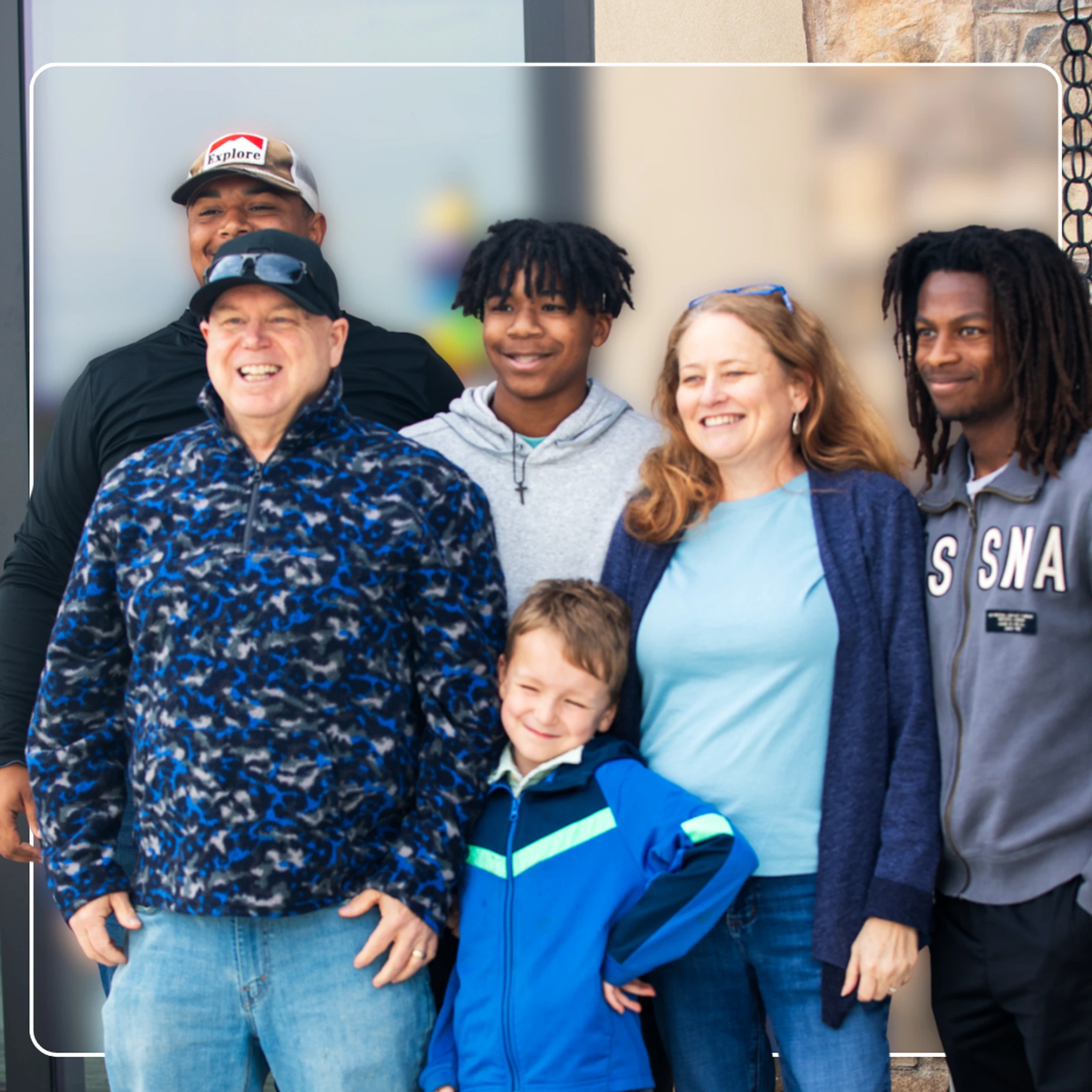 A diverse group of six people of various ages, including adults and children, smiling together for a group portrait outdoors.