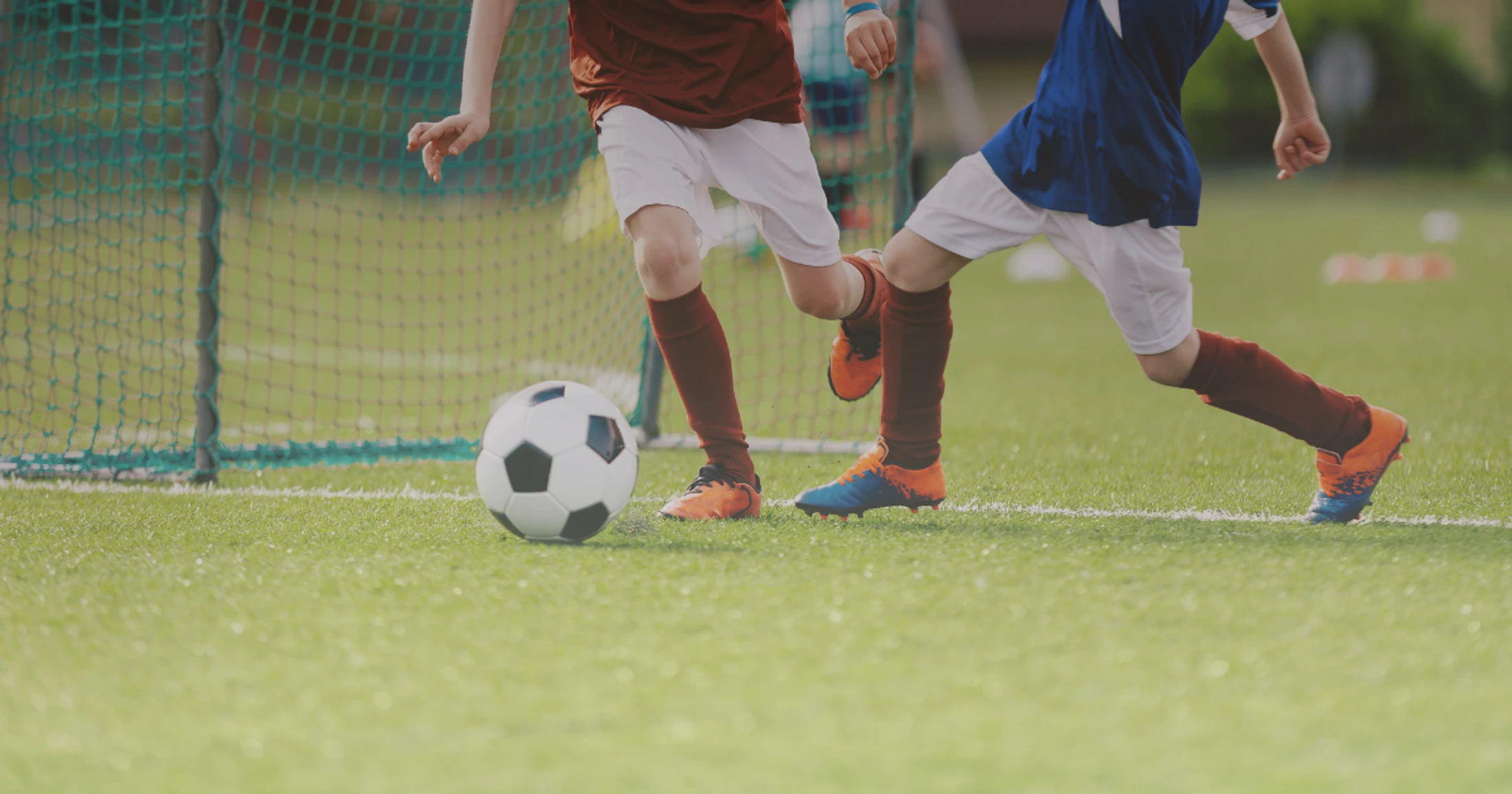 A close-up action shot of two young boys in soccer uniforms running after a soccer ball on a green turf field during a match.