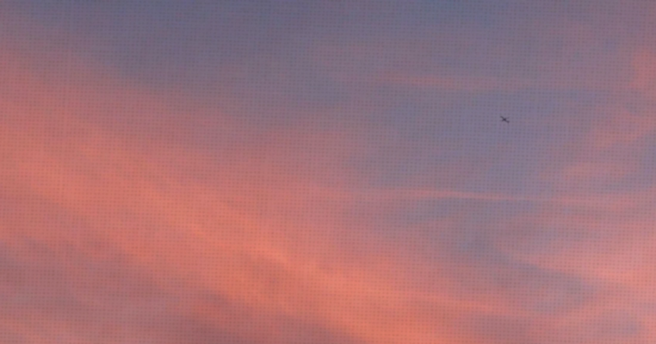 A small, distant airplane flies across a soft, pastel-colored sky filled with pink and purple clouds during sunset.