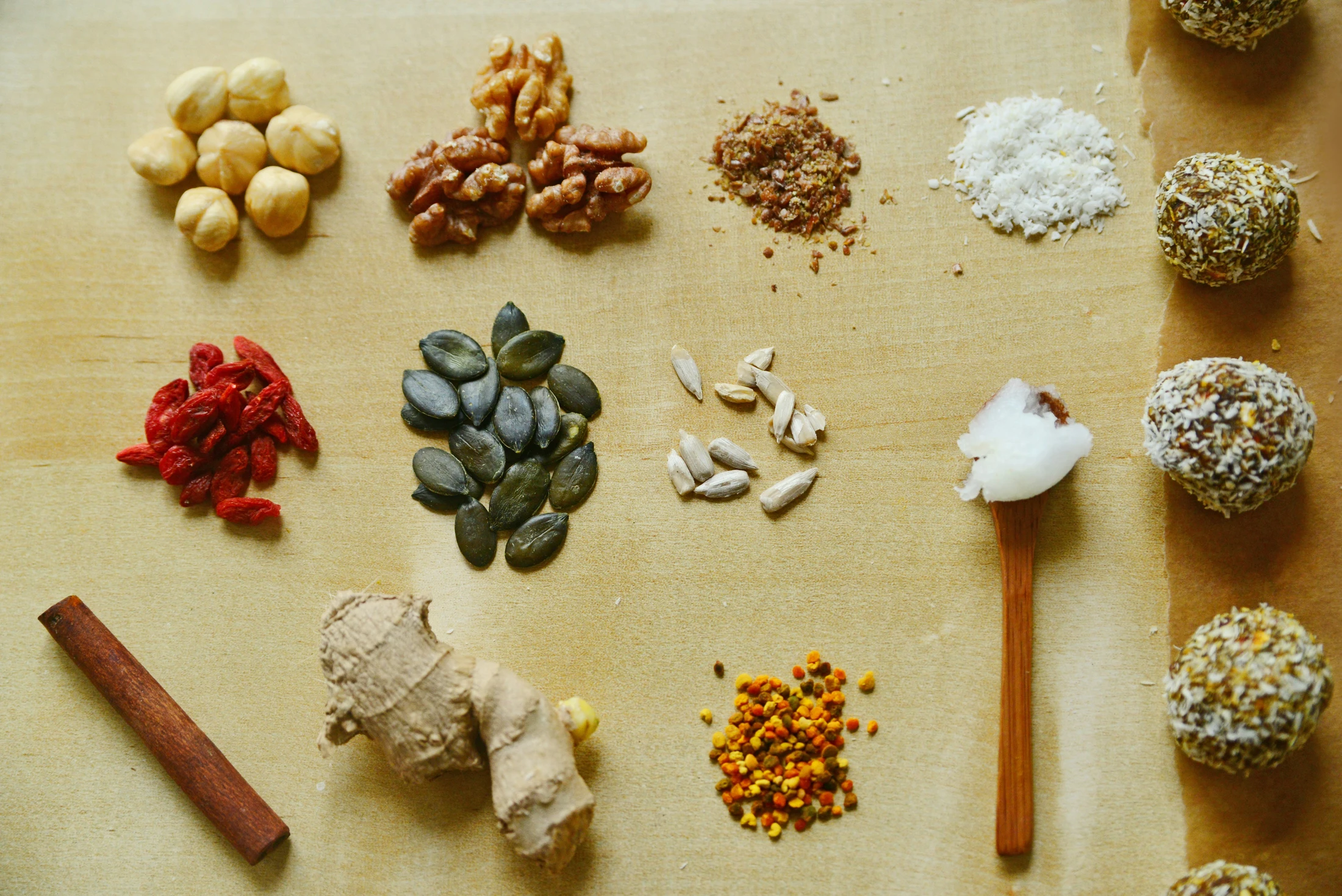 An overhead view of ingredients like nuts, seeds, goji berries, and ginger laid out next to finished coconut-covered energy balls on a wooden surface.