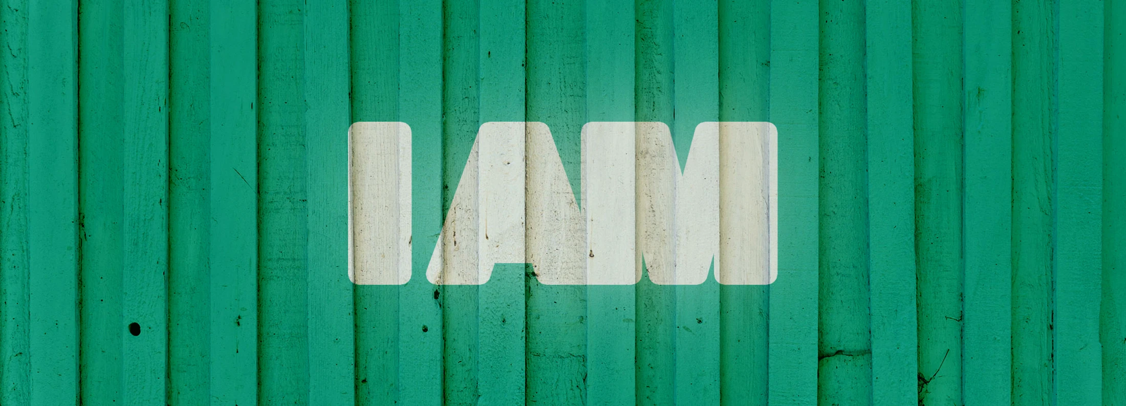 The words 'I AM' in a bold, white, textured font are centered on a background of vertical, green-painted wooden planks.