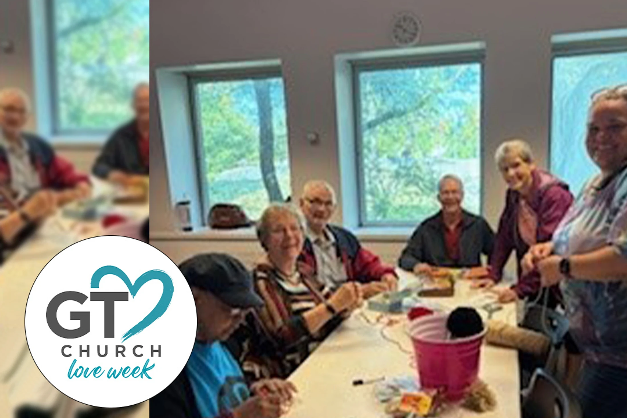 A smiling group of seniors sit at a long table indoors, crafting with colorful yarn during the GT Church Love Week event.