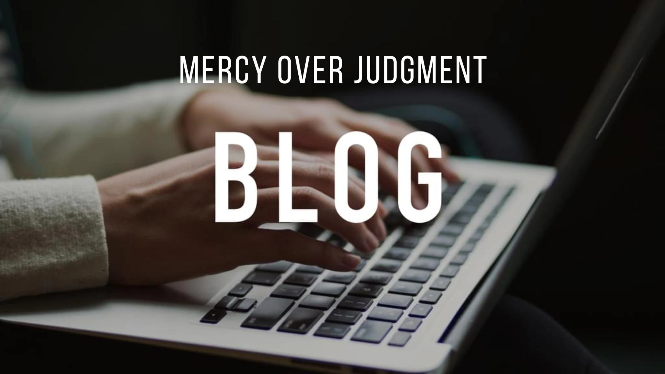 A person's hands type on a silver laptop. White text overlay reads 'Mercy Over Judgment Blog'.