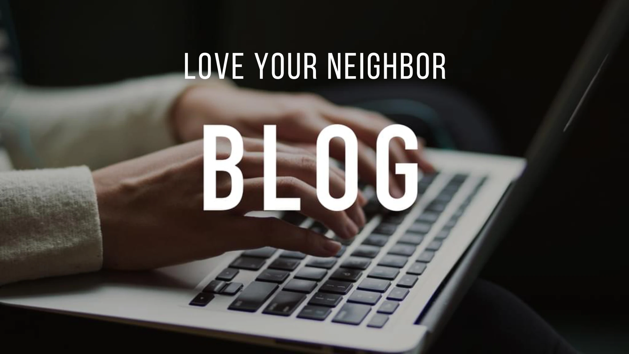A close-up of a person's hands typing on a laptop. White text is overlaid on the image that reads 'Love Your Neighbor BLOG'.