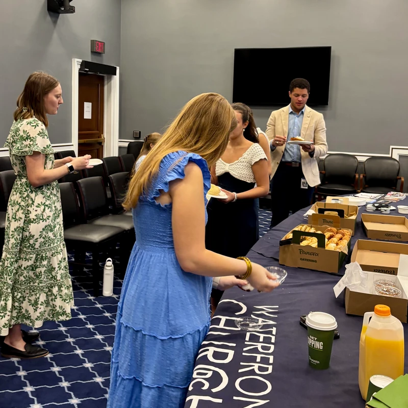 People gather around a table with Panera catering for a breakfast event hosted by Waterfront Church in a meeting room.