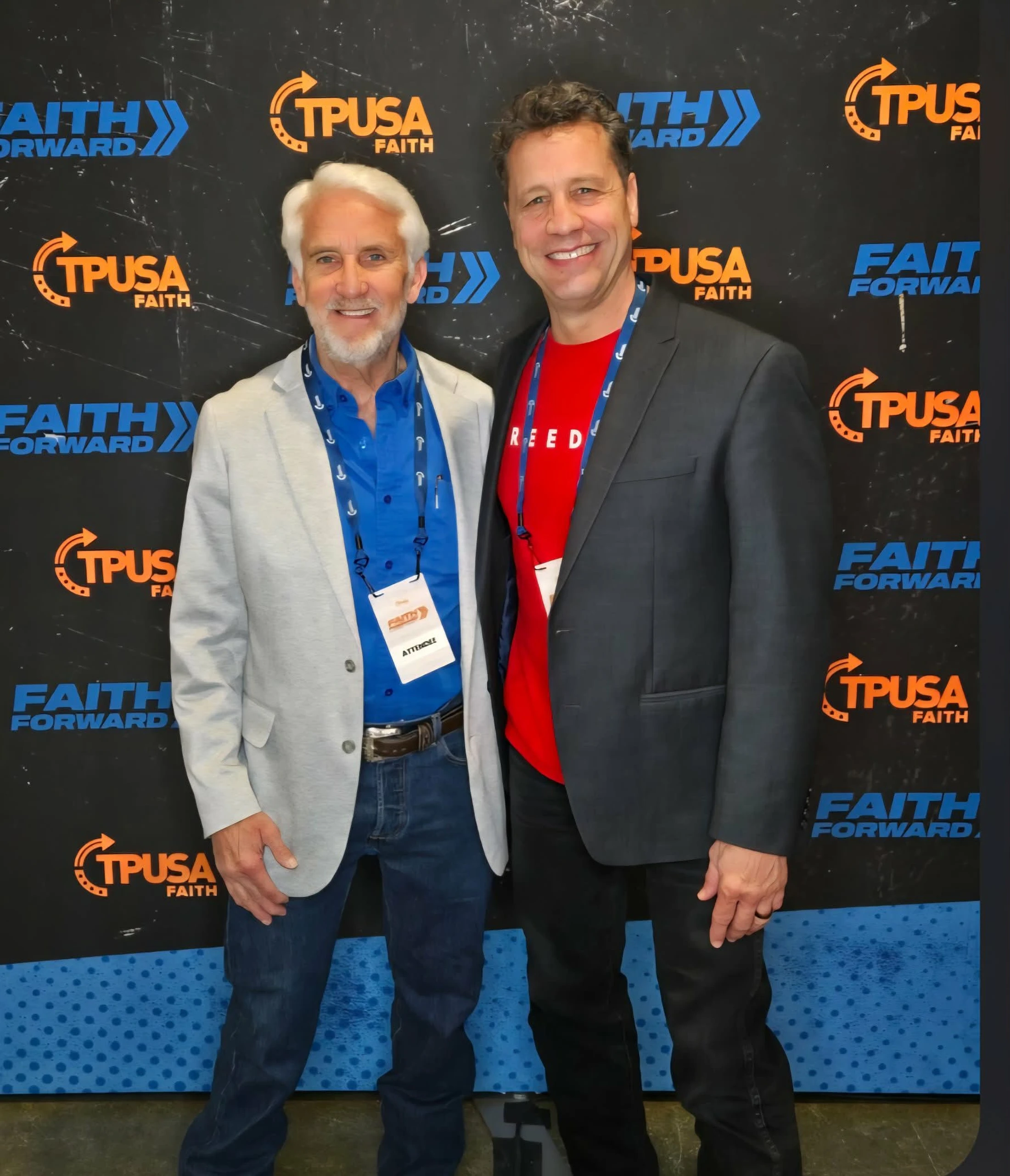 Two men smile while posing for a photo in front of a black and blue backdrop with TPUSA Faith and Faith Forward logos at a conference.