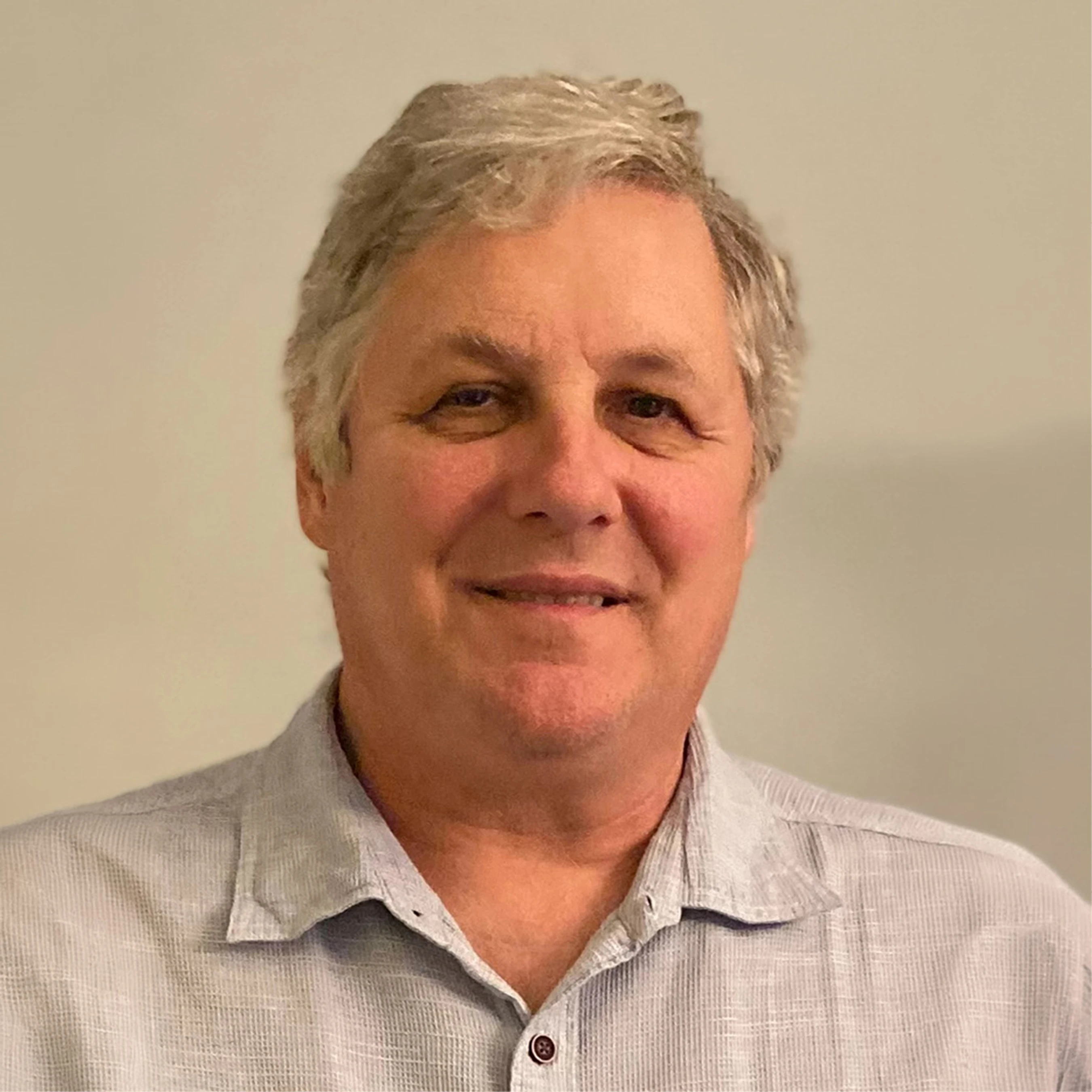 A head-and-shoulders portrait of a middle-aged man with gray hair. He is smiling slightly and looking at the camera, wearing a light blue collared shirt.