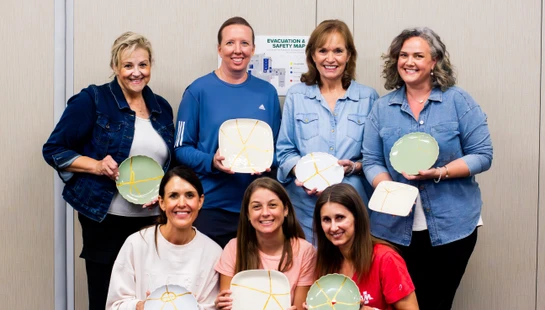 A group of seven women smile for the camera, holding up ceramic plates they have repaired with gold, a Japanese art form known as Kintsugi.