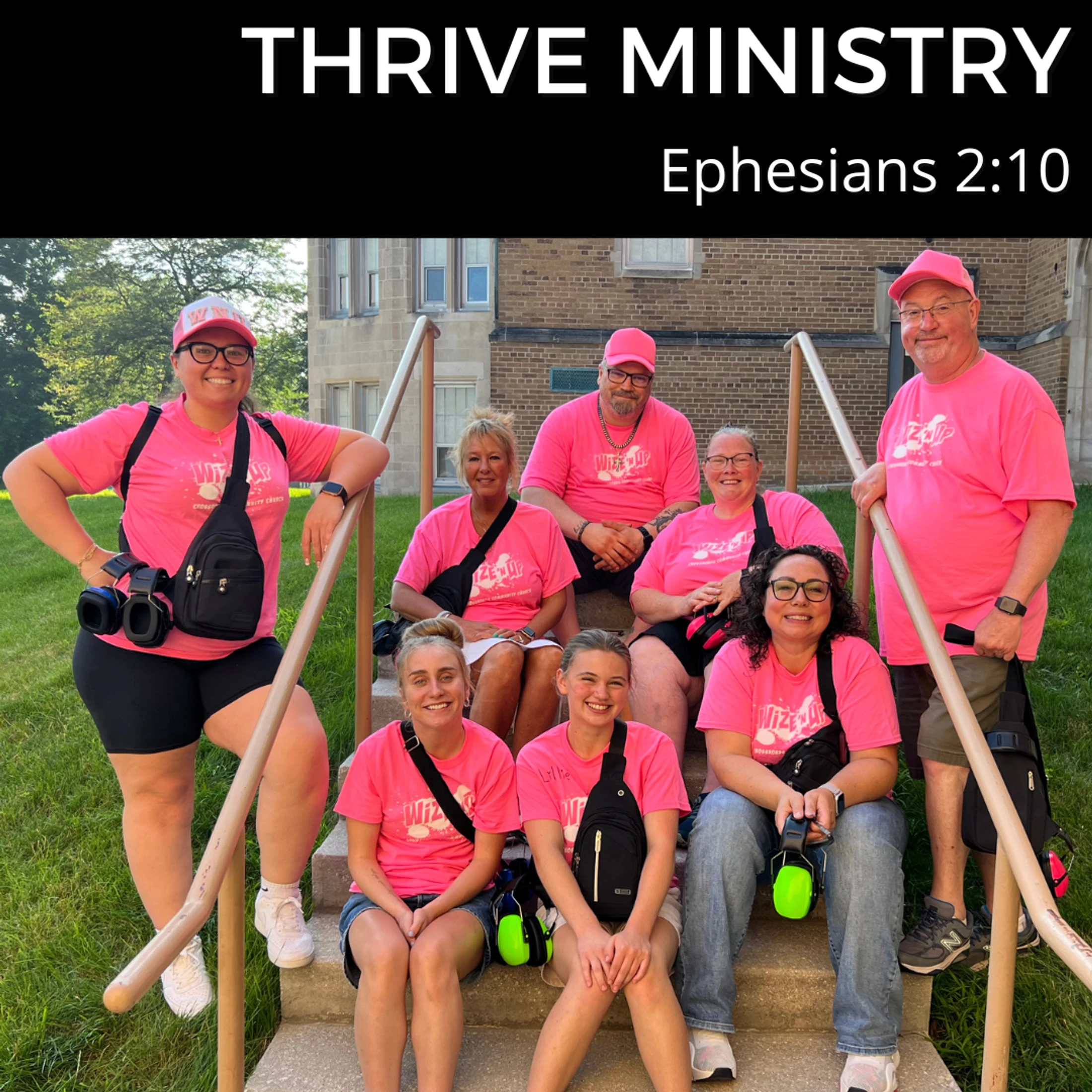 A group of eight people from Thrive Ministry wearing matching pink t-shirts and smiling while posing for a photo on outdoor steps.