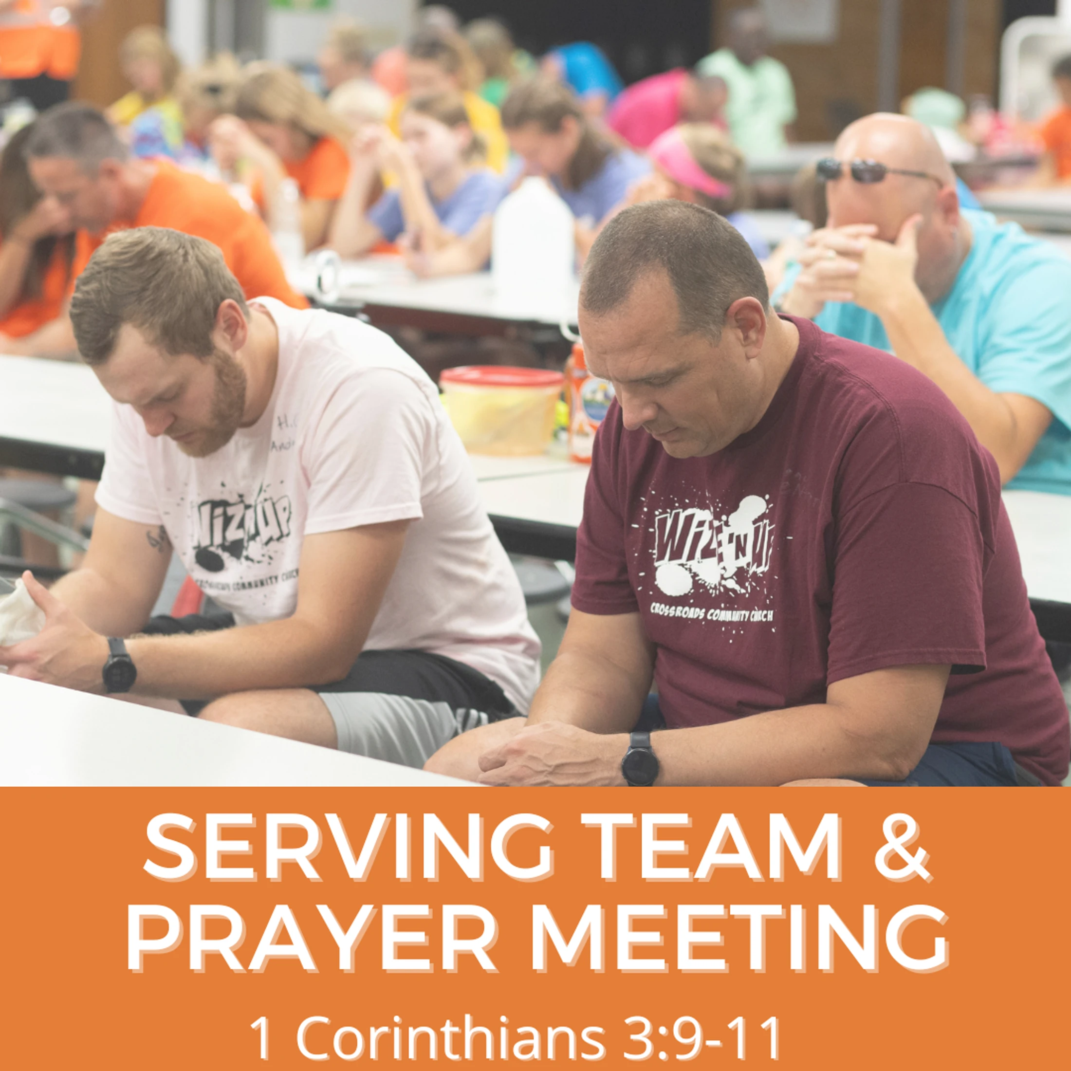 A group of people sit at long tables with their heads bowed in prayer. The foreground focuses on two men in prayer.