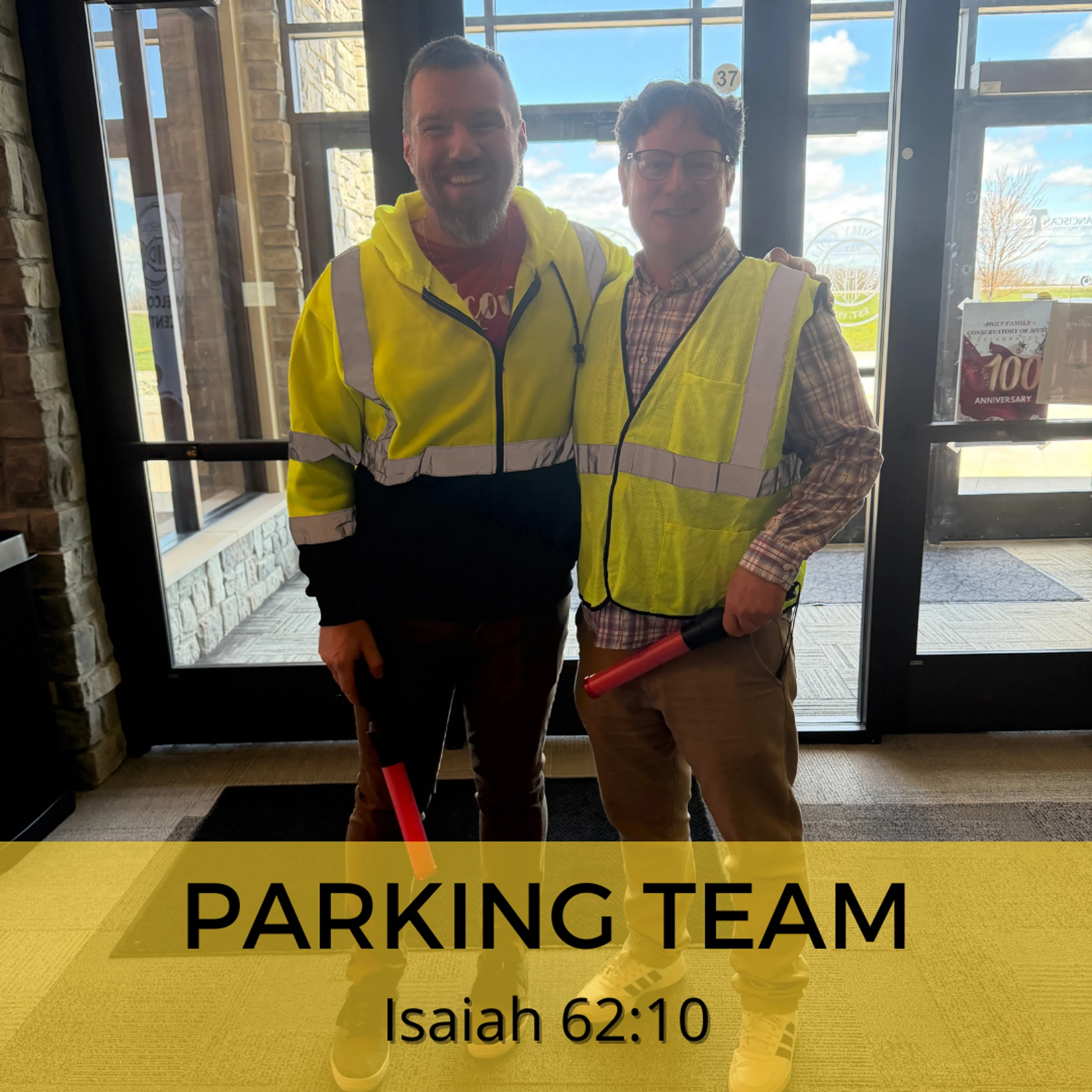 Two smiling men in yellow high-visibility vests stand inside by glass doors, holding red traffic wands, with text overlay reading 'Parking Team'.