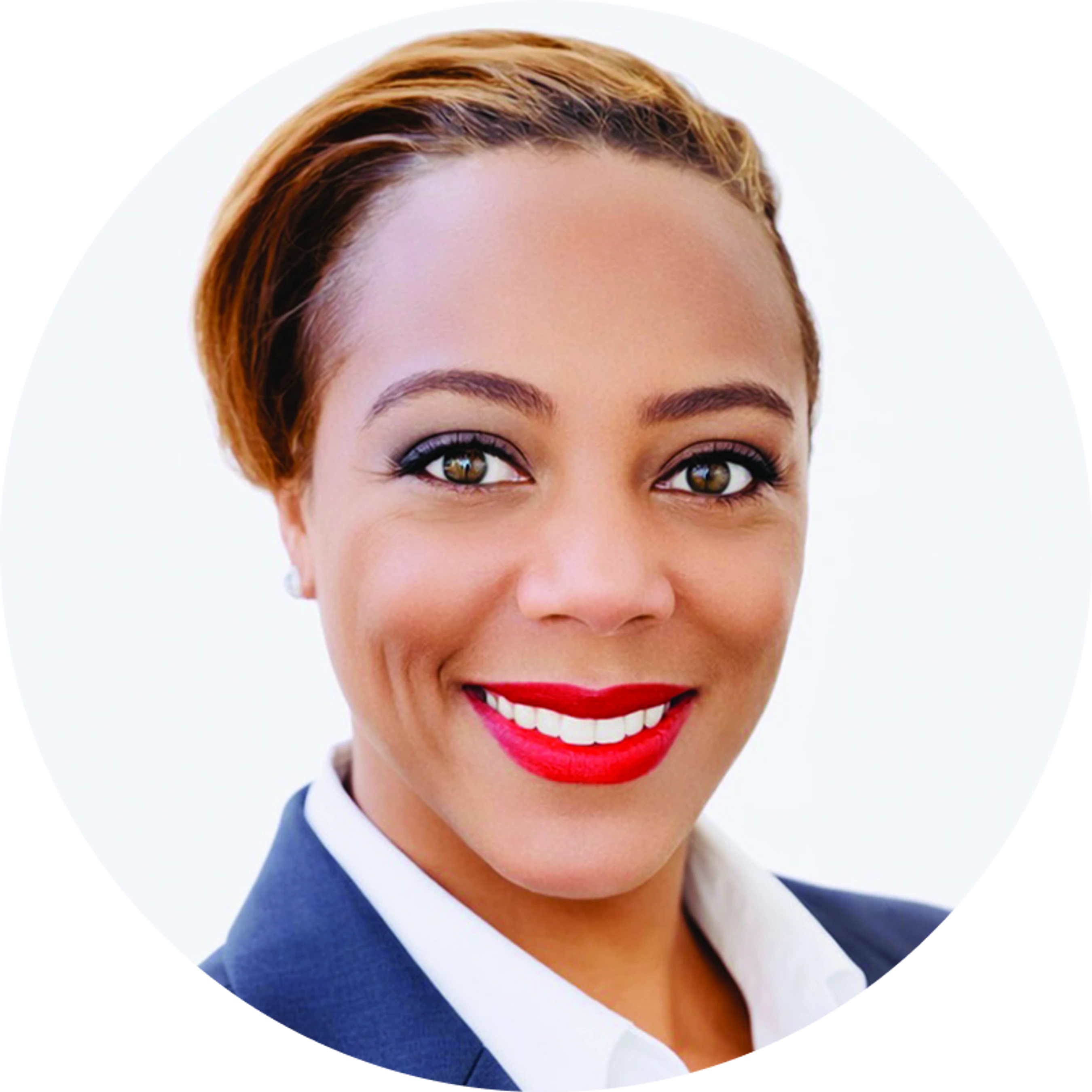 A circular headshot of a smiling woman with short, light-brown hair, wearing red lipstick, a white collared shirt, and a dark blazer against a white background.