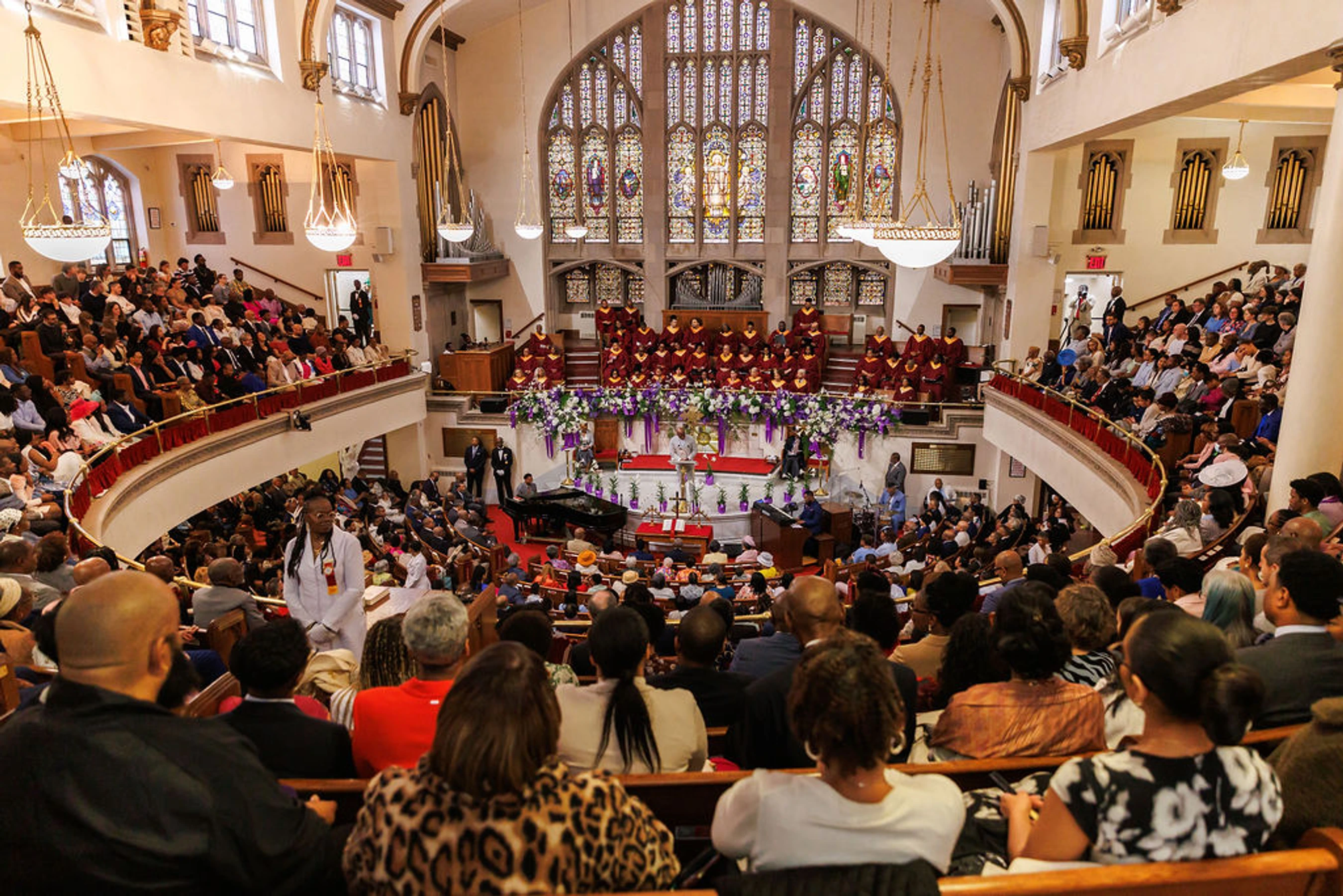 A high-angle view of a large, ornate church filled with a diverse congregation during a service, with a choir in red robes at the front.