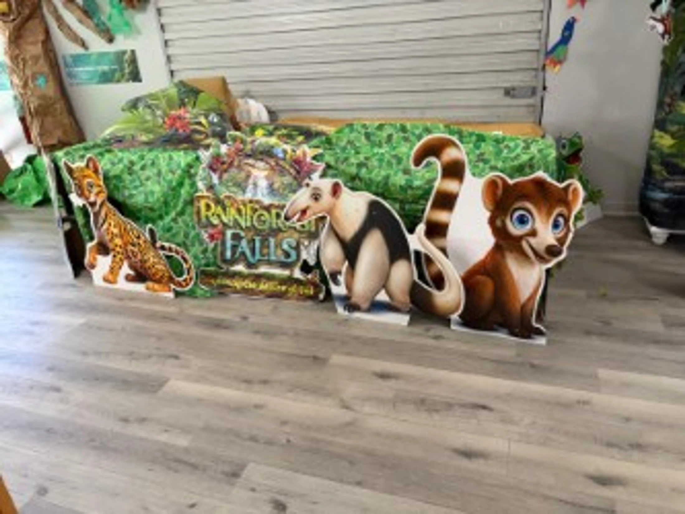 Cardboard cutouts of cartoon animals, including an ocelot and an anteater, in a room decorated with a jungle theme for a 'Rainforest Falls' event.