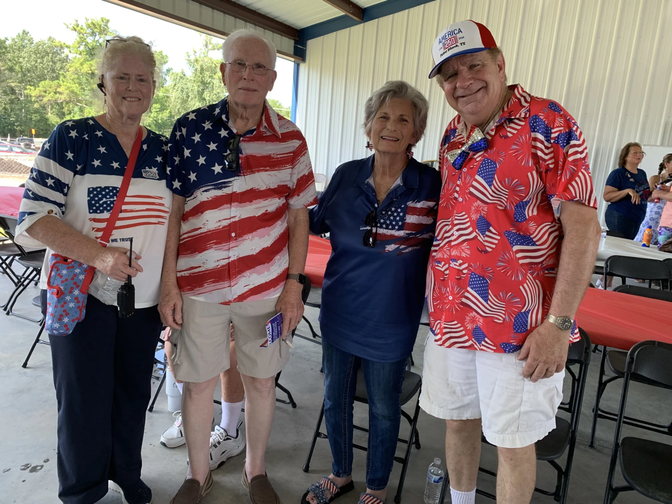 Four smiling seniors, two men and two women, stand together wearing various red, white, and blue American flag-themed shirts at an outdoor gathering.