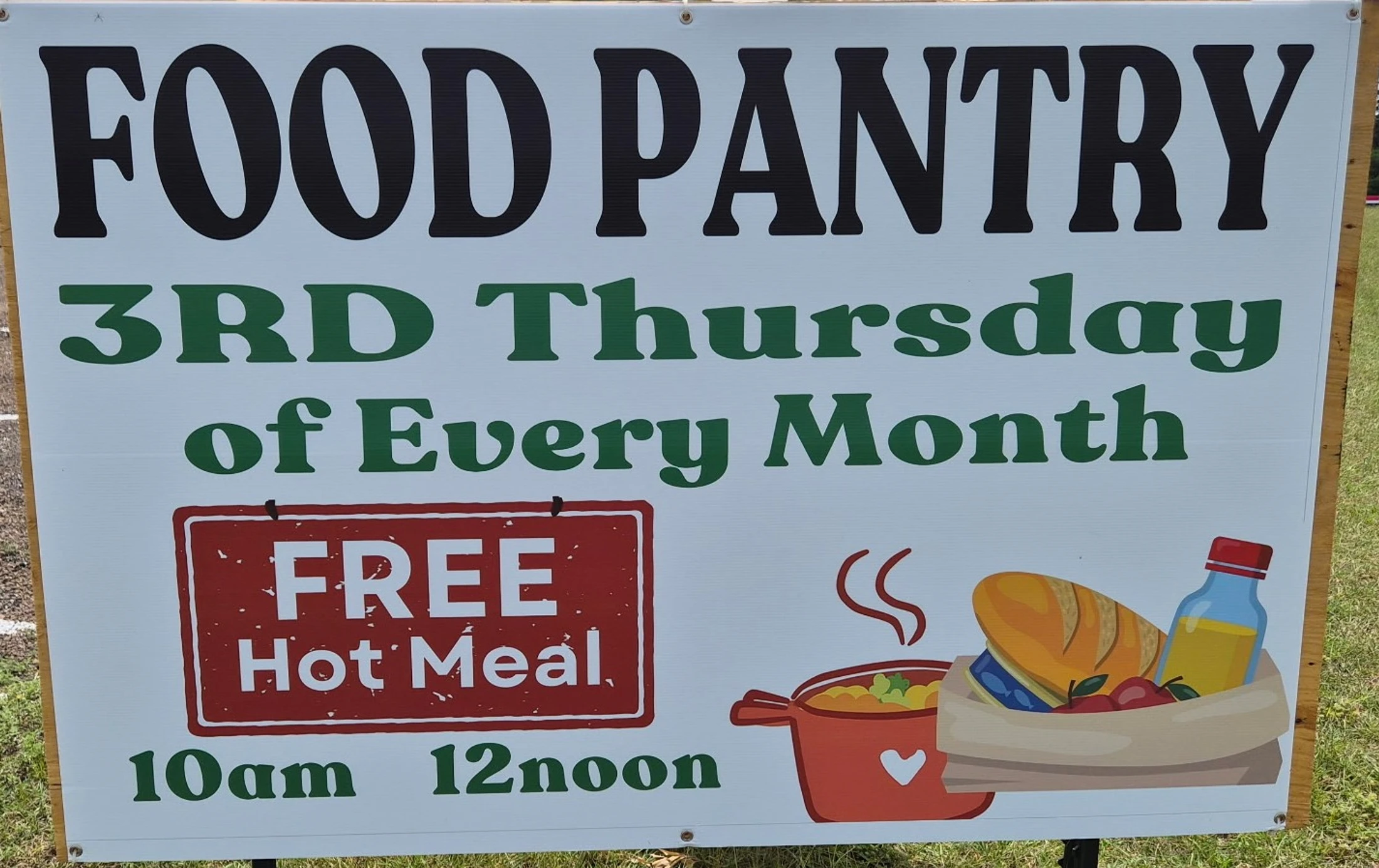 A white sign for a food pantry, advertising a free hot meal on the third Thursday of every month from 10am to 12noon.