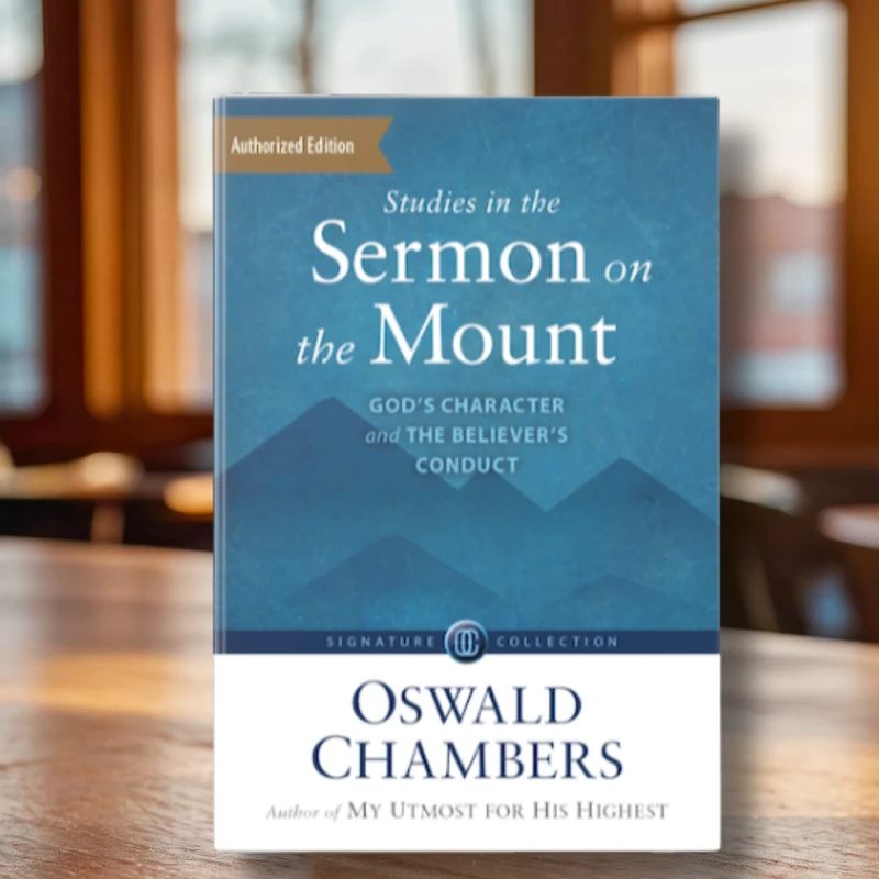 A copy of the book 'Studies in the Sermon on the Mount' by Oswald Chambers standing upright on a wooden table in a warmly lit room.