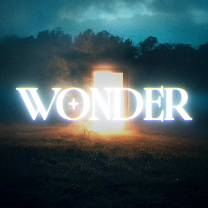 The word 'WONDER' glows in white letters over a mysterious, brightly lit doorway standing in a dark, misty field at night.