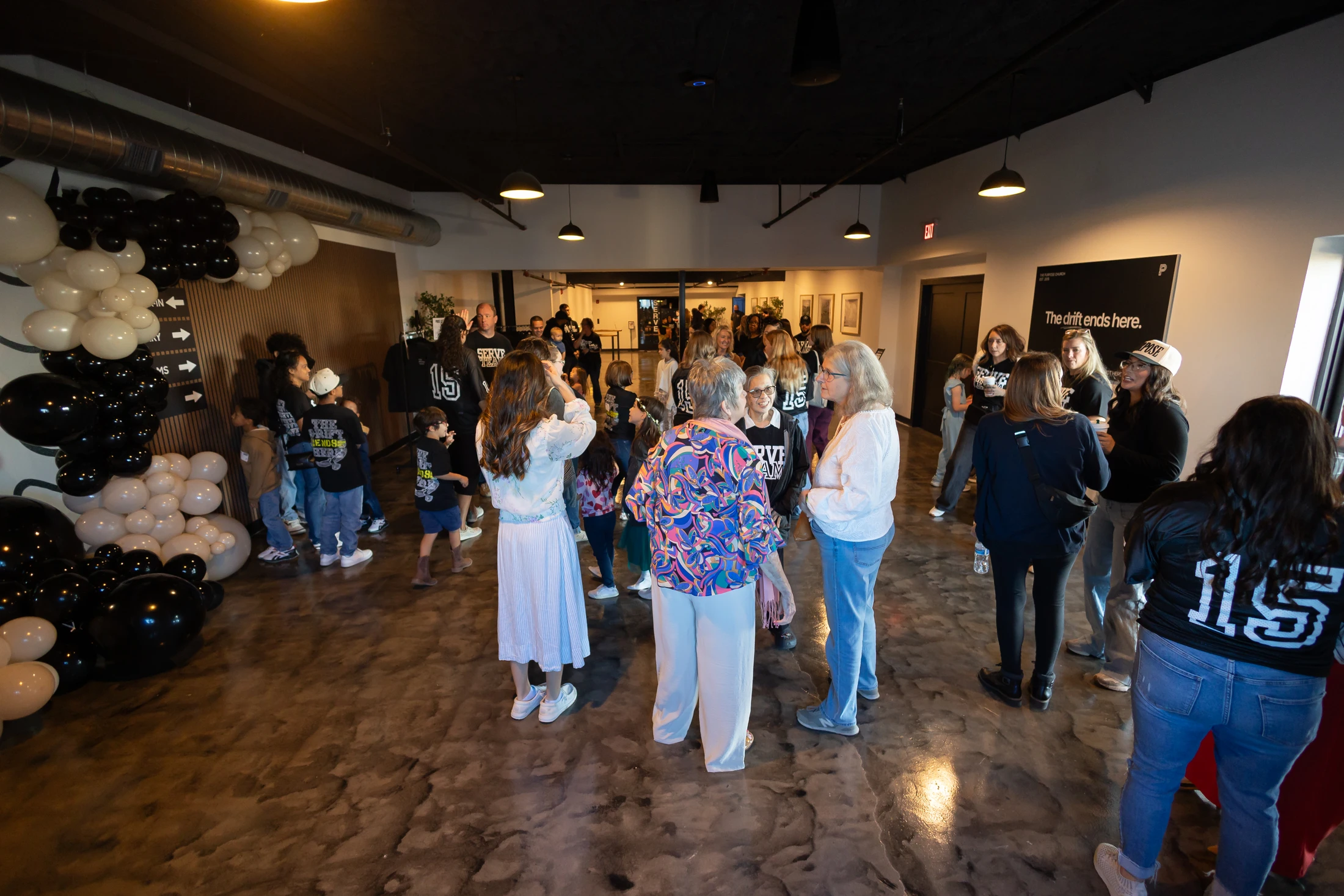 A wide-angle shot of a diverse group of people socializing in a modern event space, with black and white balloon decorations on the left wall.