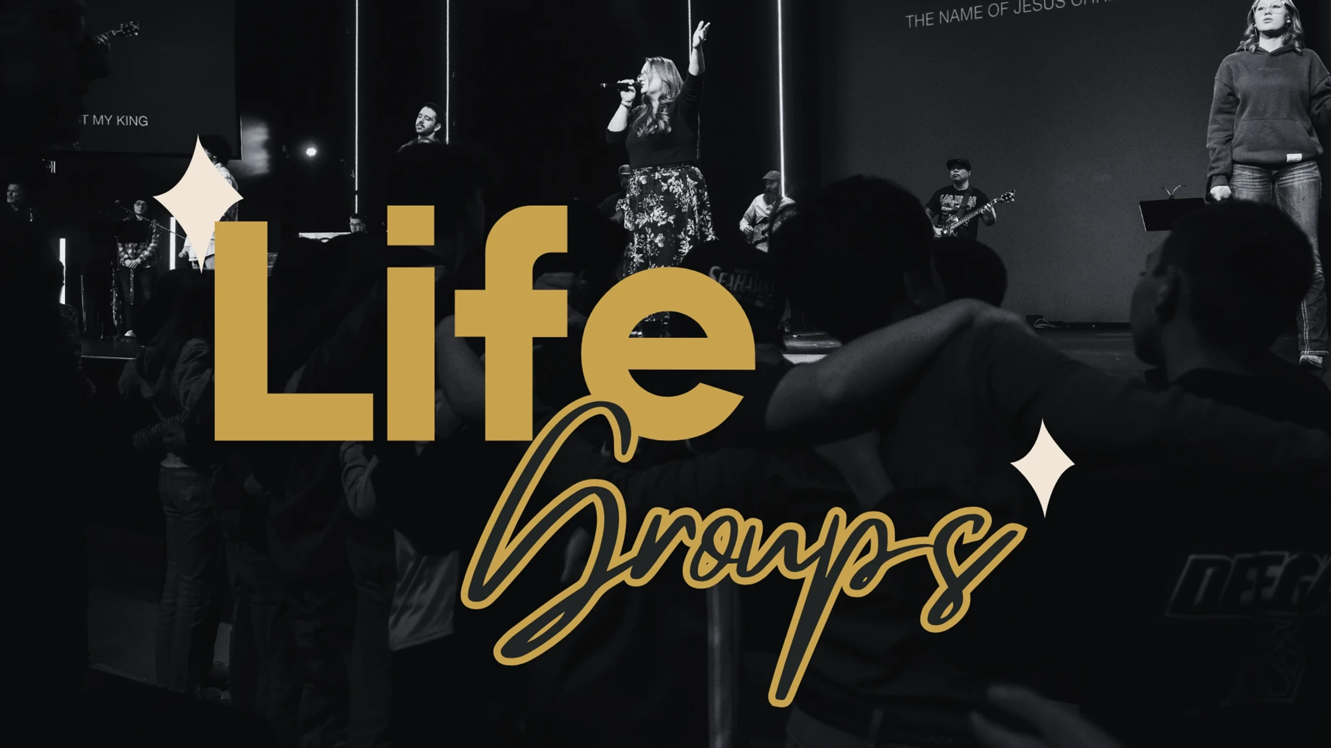 A black and white photo of a church service with a band on stage and people worshipping. Bold gold text overlay reads 'Life Groups'.