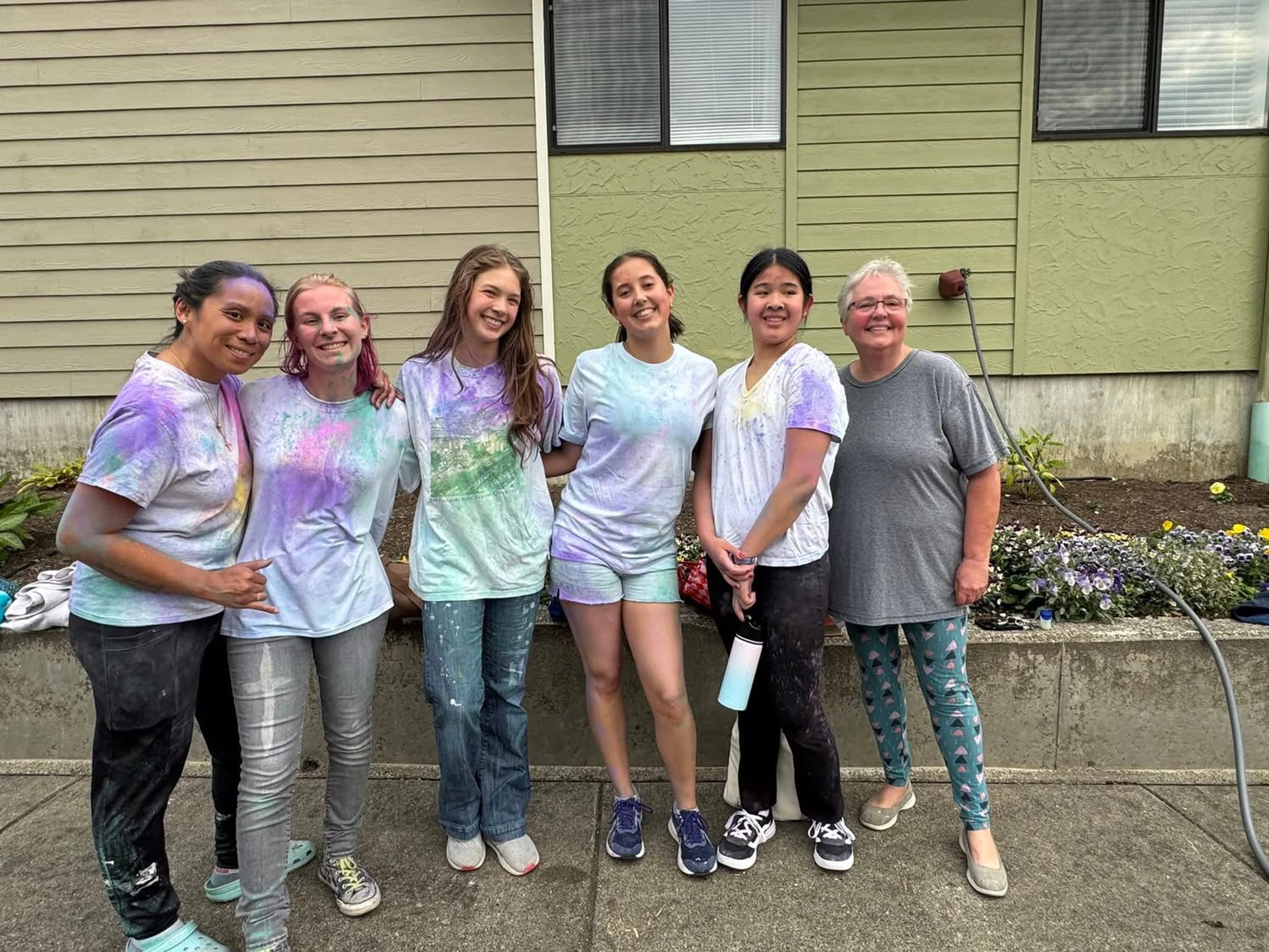 A group of six smiling women and girls of different ages pose for a photo, their clothes and faces spattered with purple and blue colored powder.