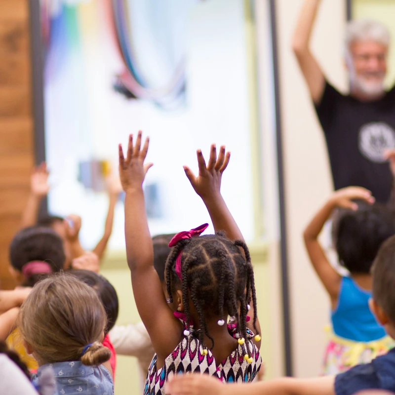 Children energetically raise their hands in a Kids Ministry classroom at Redeemer Alliance Church, a Christian Church in Robbinsville, NJ, as a teacher guides the lesson.