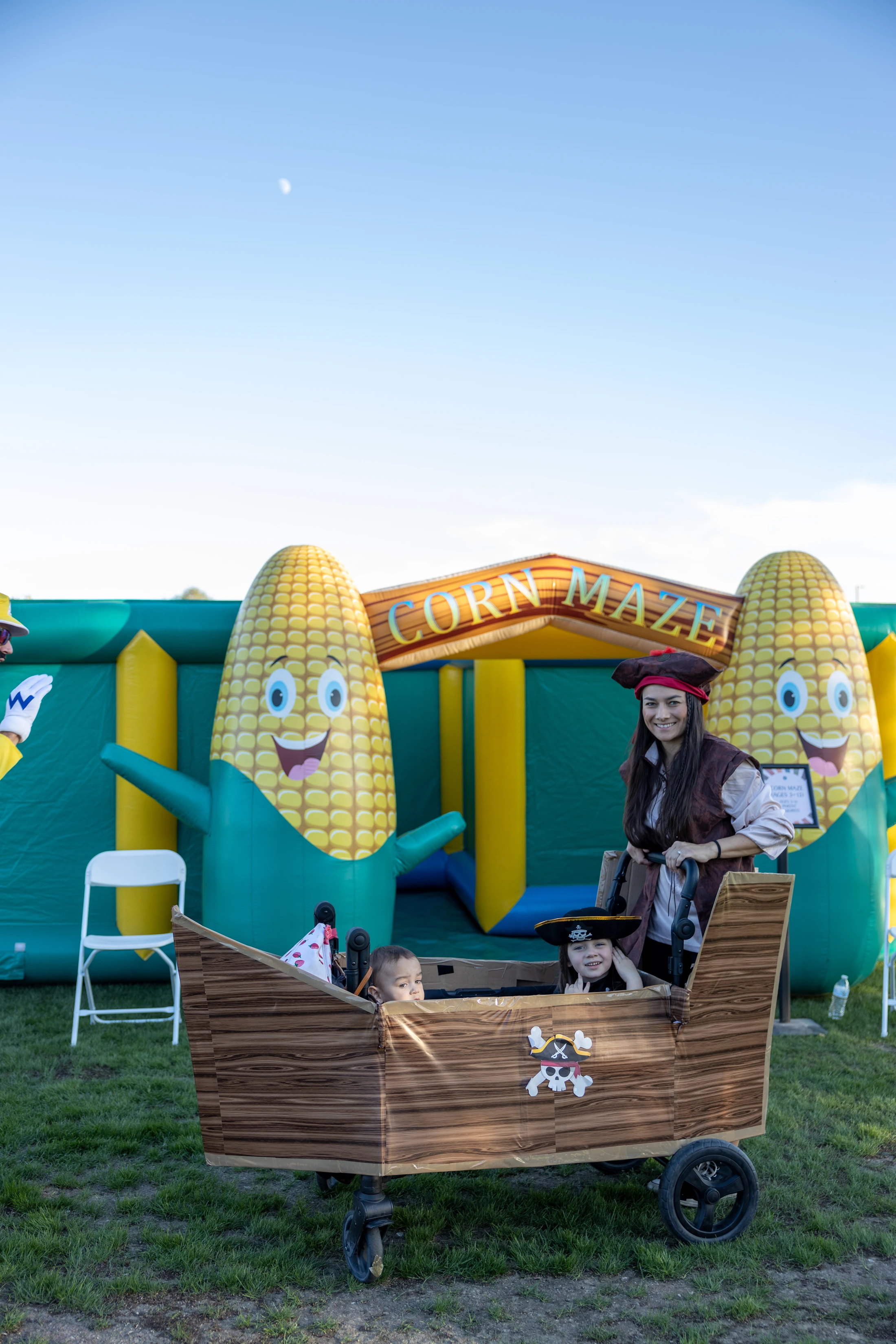A woman and two children dressed as pirates pose with a wagon decorated like a pirate ship in front of an inflatable corn maze.