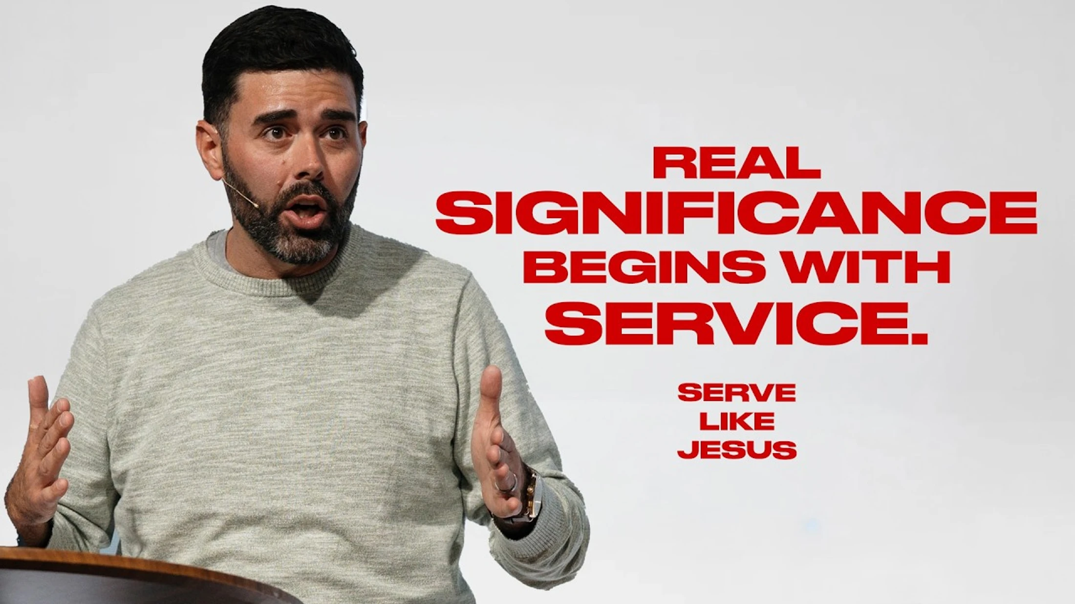 A man speaks at a podium with red text beside him reading, "Real significance begins with service. Serve like Jesus."