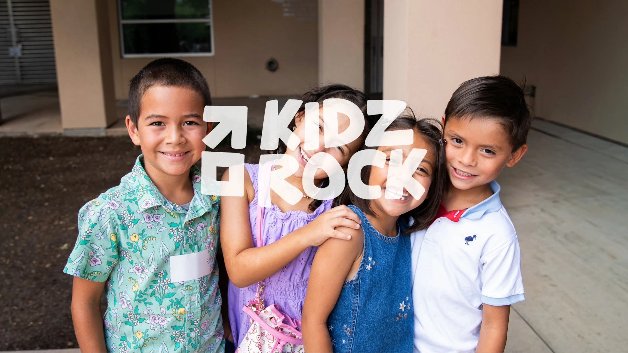 A group of four smiling elementary school-aged children, two boys and two girls, standing close together outdoors. A white text overlay reads 'Kidz Rock'.