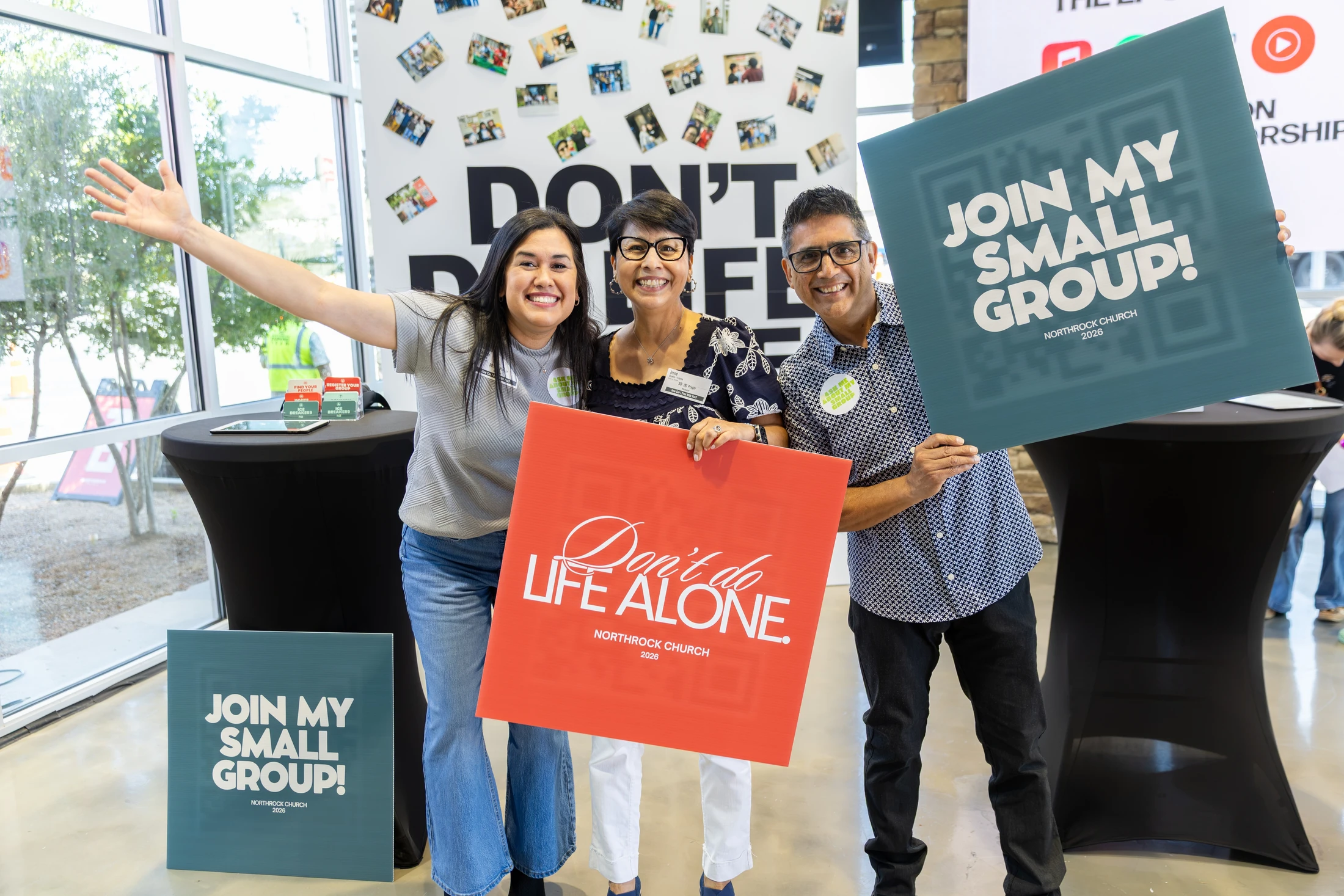 Three smiling church members hold signs inviting people to join a small group. One sign reads 'Don't do life alone,' another says 'Join my small group!'