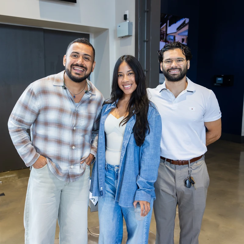 A woman stands between two men as they all smile for the camera in a modern building lobby with a staircase and a map graphic in the background.