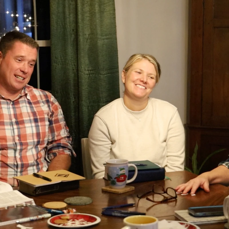 LifeGroup members gathered around a table, smiling and talking over coffee with Bibles and notebooks open.