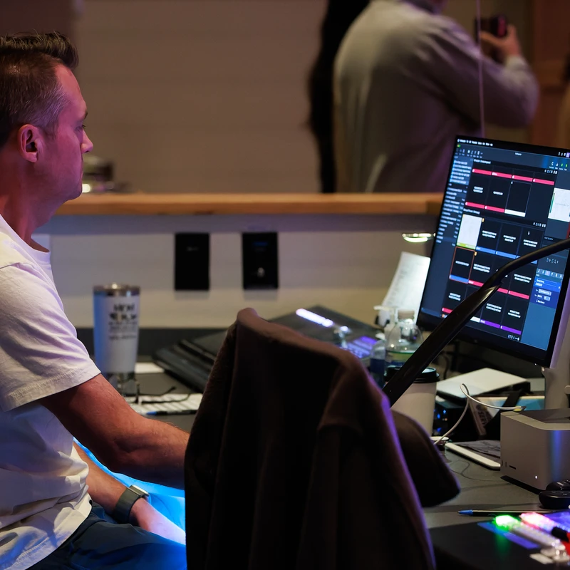 Volunteer sitting at the tech booth, monitoring worship service visuals and audio on multiple screens.