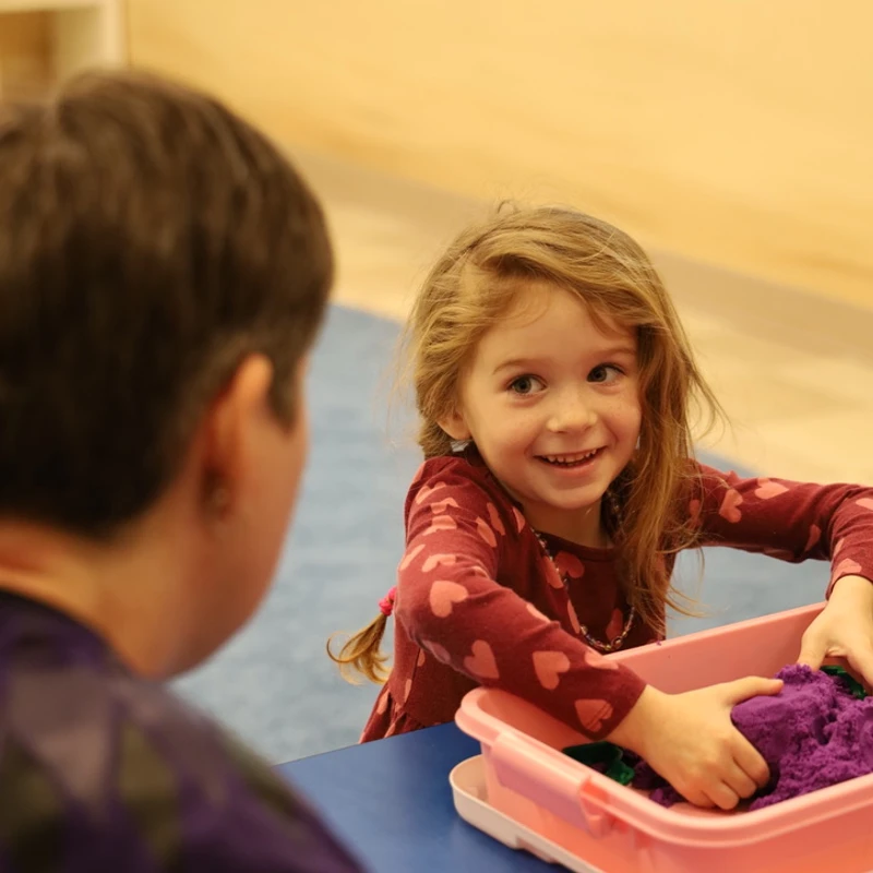 A smiling girl plays with colored sensory sand at a children's ministry table at The Crossing in Milton, DE.