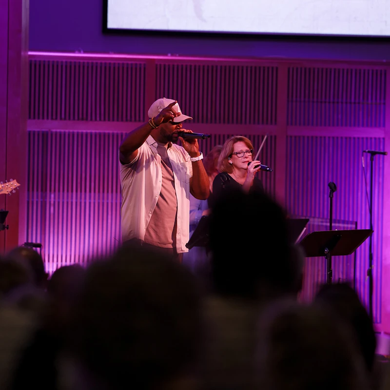 Worship band performing on stage with purple lighting and projected lyrics at The Crossing