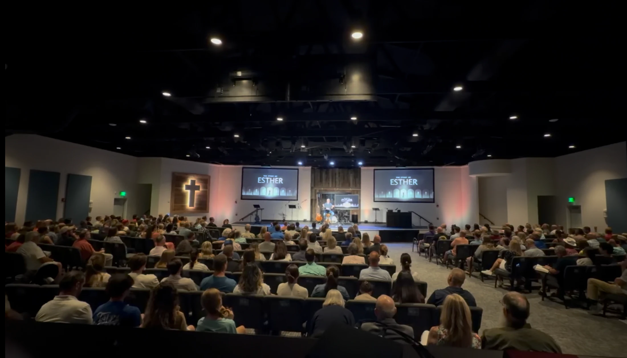 A wide shot from the back of a modern church auditorium filled with a large congregation watching a service about 'The Story of Esther' on stage.