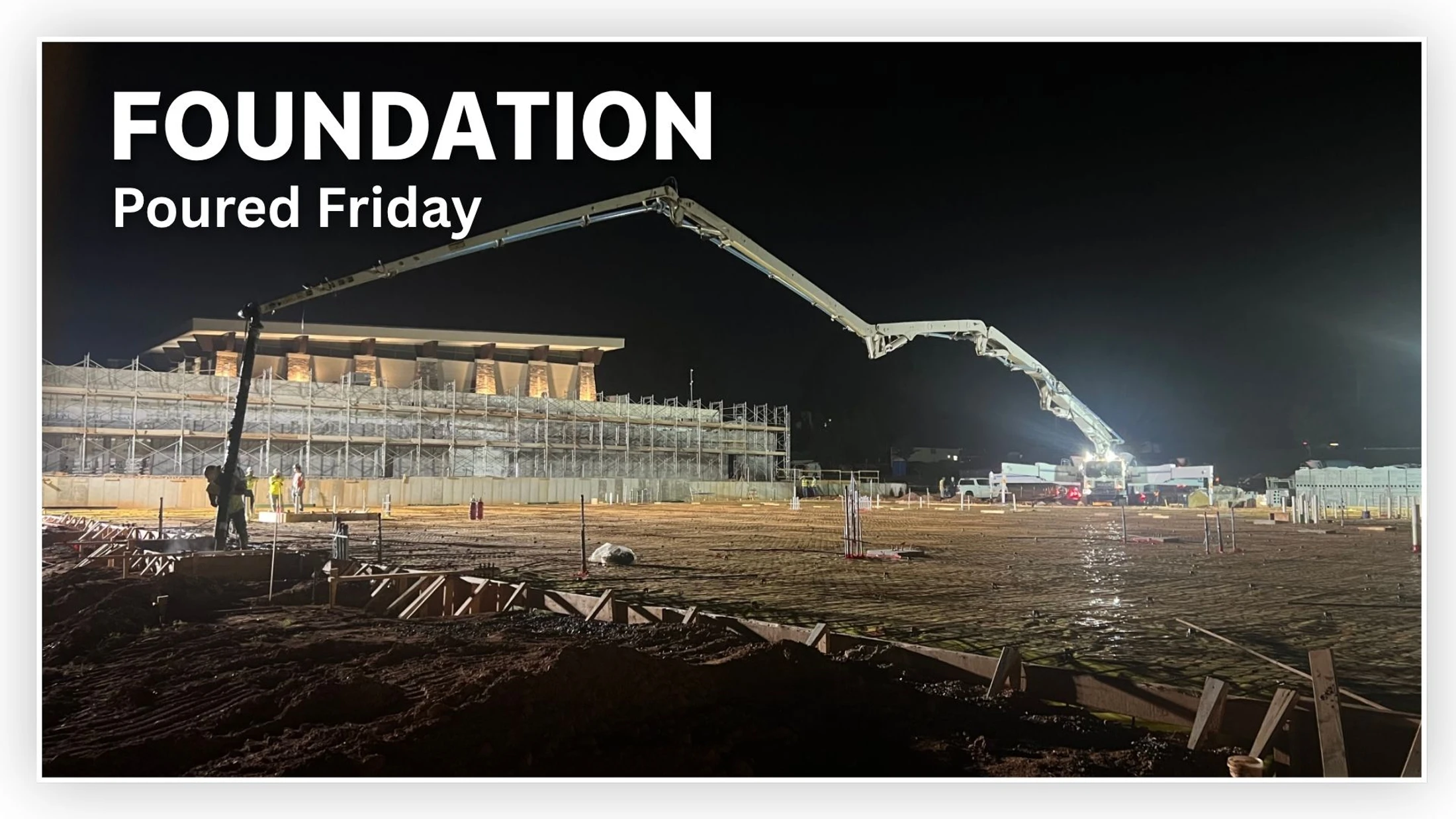 A large construction site at night, brightly lit. A concrete pump truck with a long boom extends over an area where the foundation is being poured.