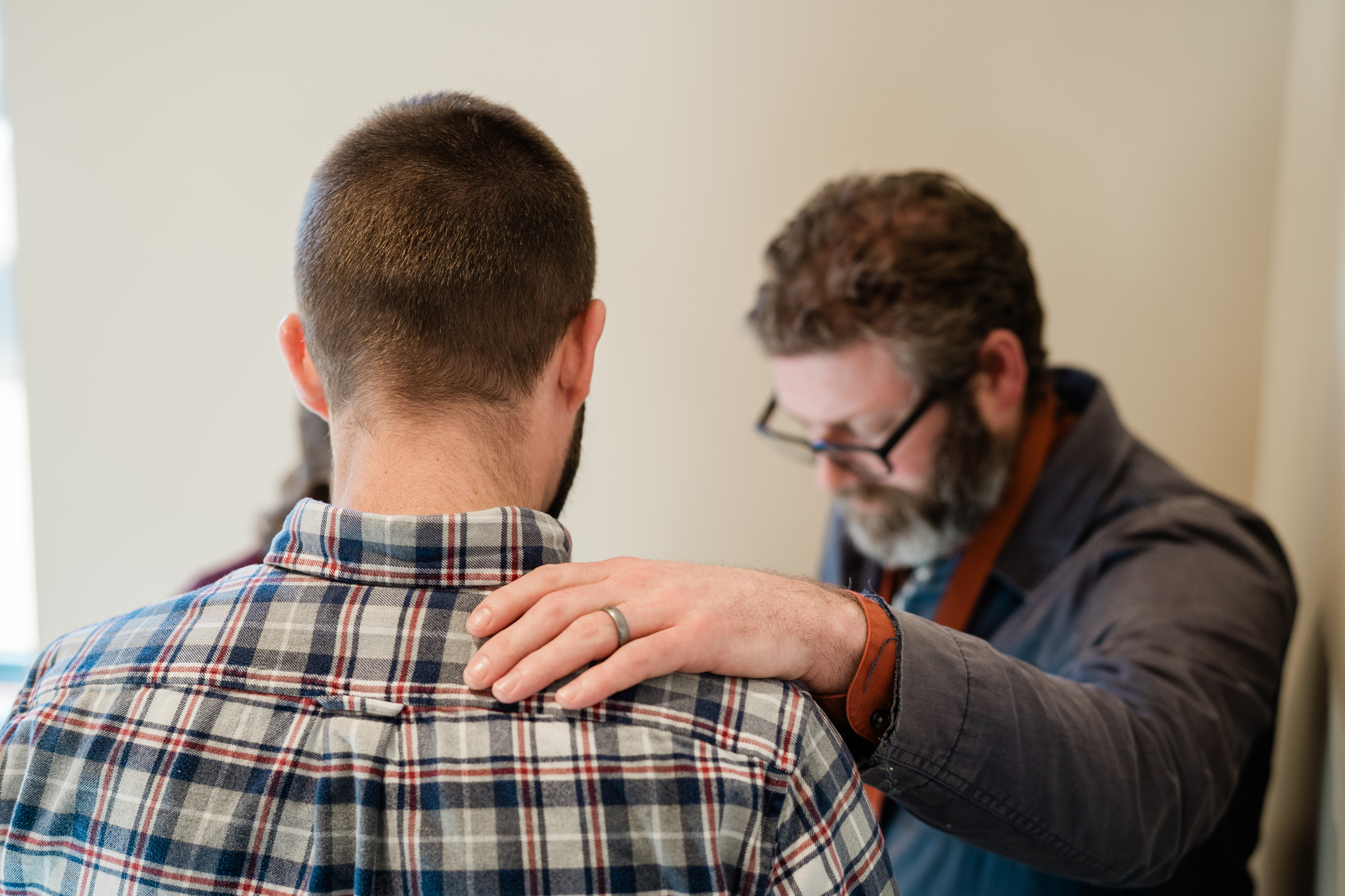A person praying with a hand resting gently on another person's shoulder.