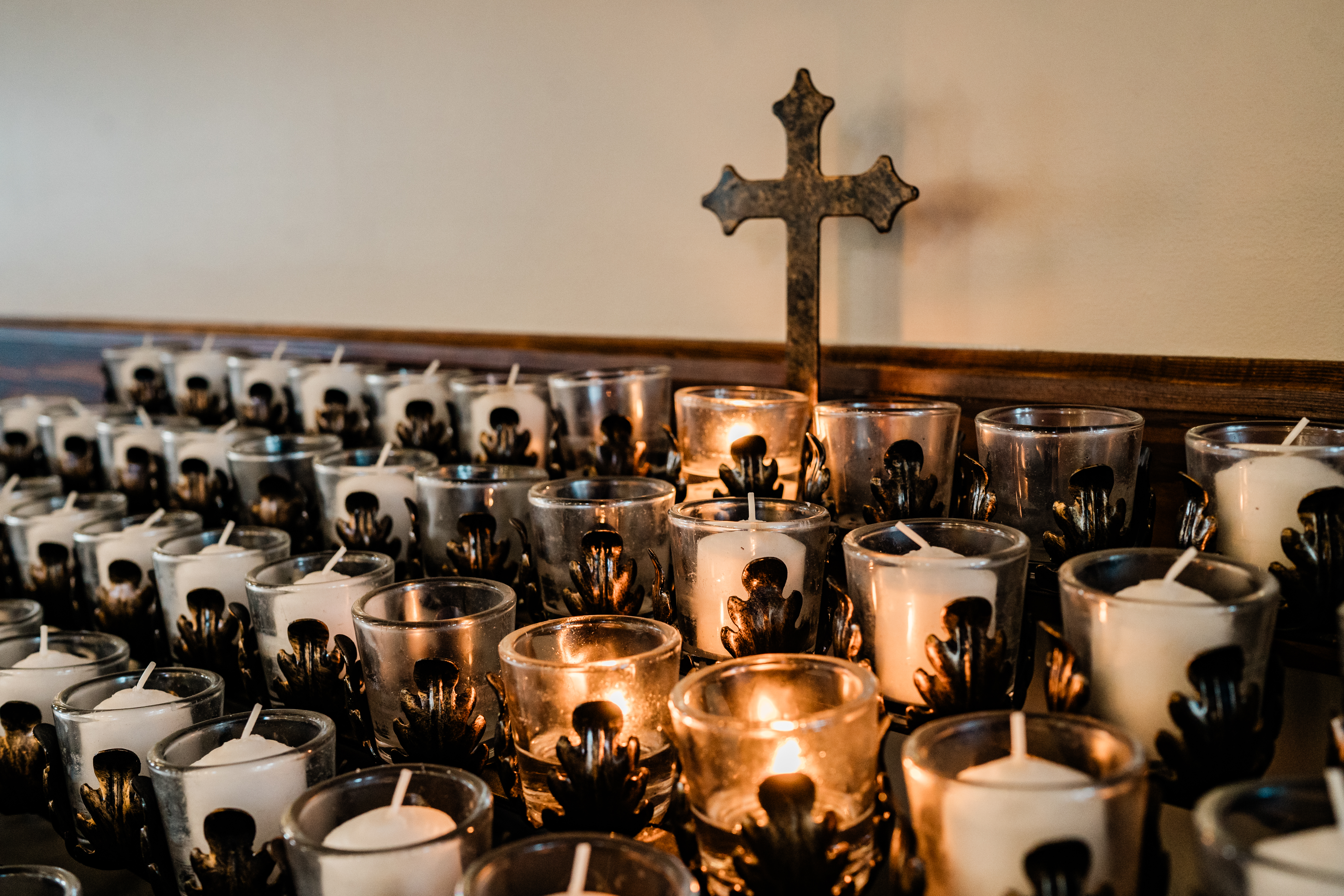 Lit prayer candles gathered beneath a cross.