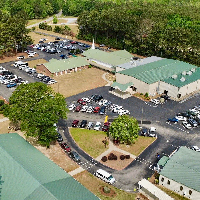 An aerial photograph shows a large church complex with several green-roofed buildings surrounded by trees. The parking lots are filled with many cars.