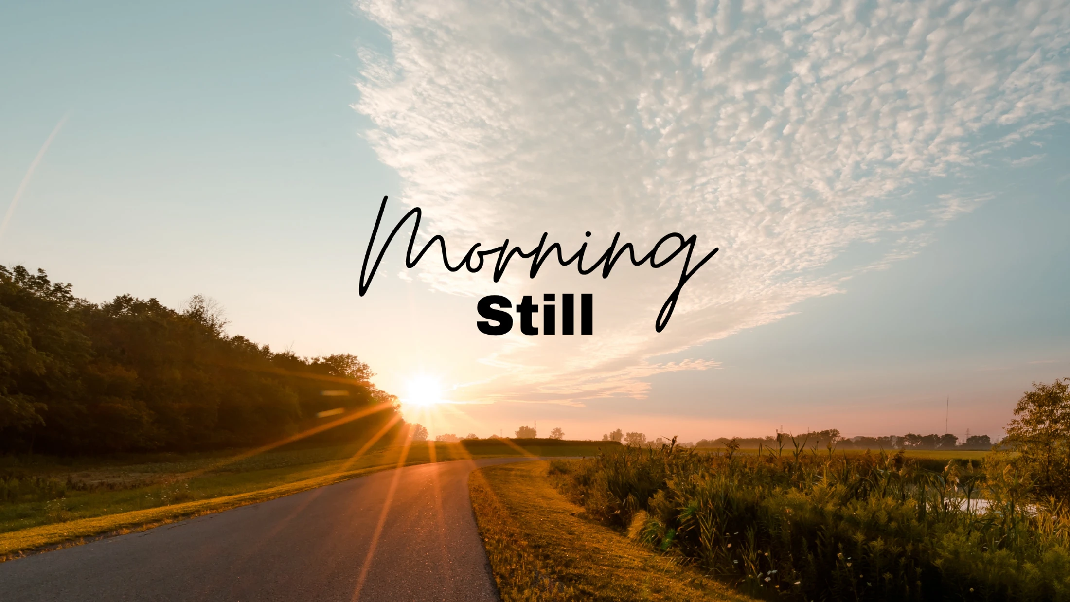 The sun rises over a quiet country road. The text 'Morning Still' is overlaid on the image of the sky, trees, and a field.