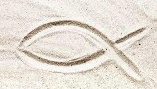 A simple drawing of the Ichthys, or Christian fish symbol, etched into the surface of light-colored sand.