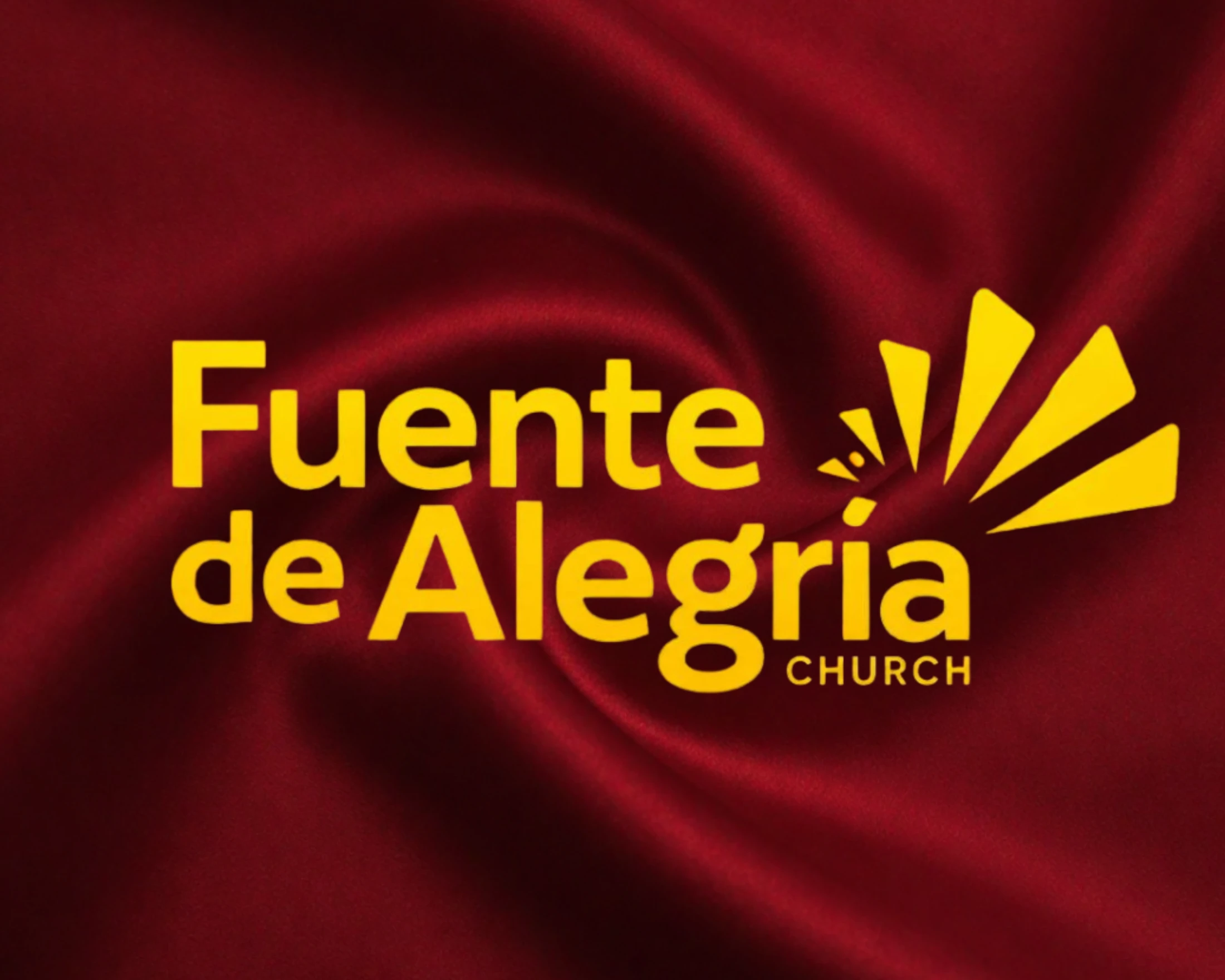 The logo for Fuente de Alegria Church in yellow text on a deep red, silk-like background. A stylized sunburst graphic is next to the text.