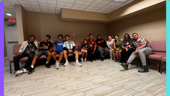 A diverse group of smiling adults and teenagers from the FDA Jóvenes youth group sitting together on chairs in a brightly lit room, posing for a photo.