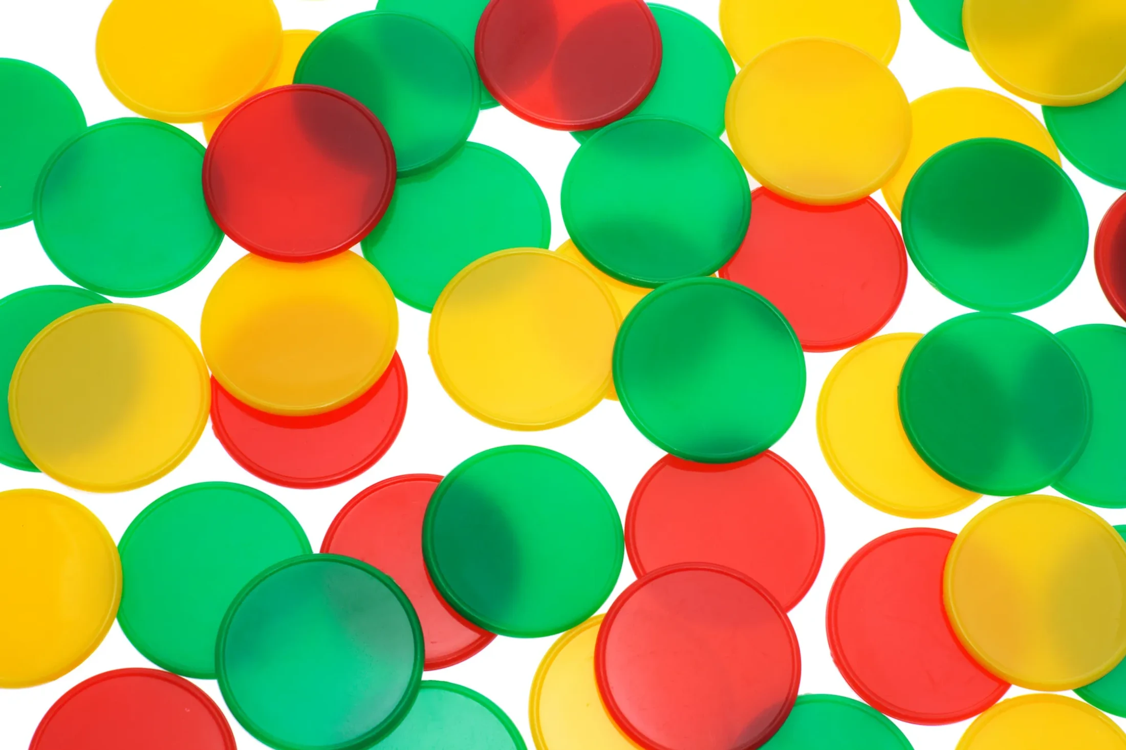 A top-down view of red, yellow, and green translucent plastic circular counters scattered and overlapping on a solid white background.