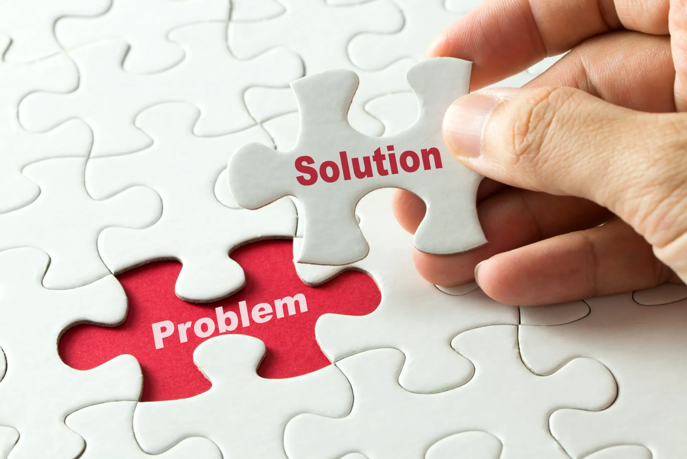 A hand places a puzzle piece labeled 'Solution' into a missing spot labeled 'Problem' on a white puzzle, symbolizing finding a solution to a problem.