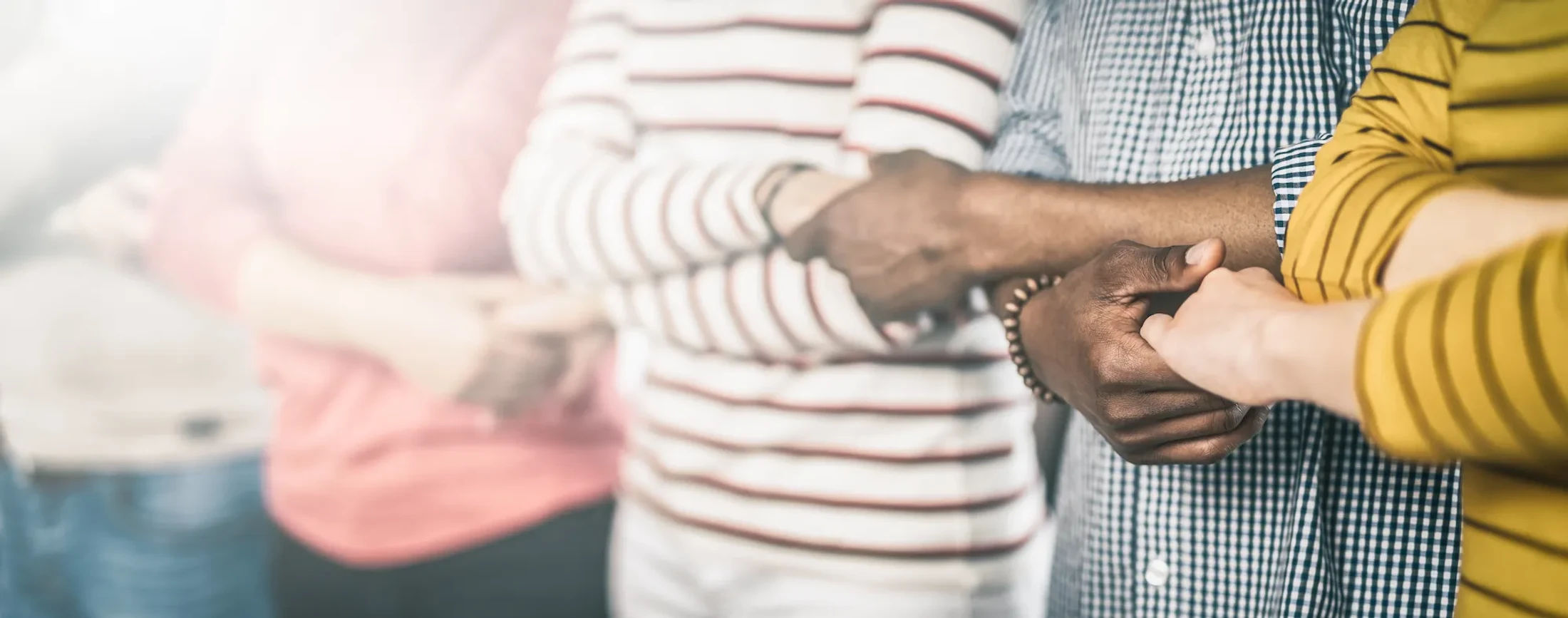 A close-up of a diverse group of people standing in a row and linking arms, a symbol of unity, support, and community.