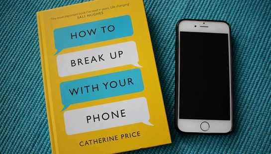 A yellow book titled 'How to Break Up With Your Phone' by Catherine Price lies next to a smartphone on a blue textured surface.